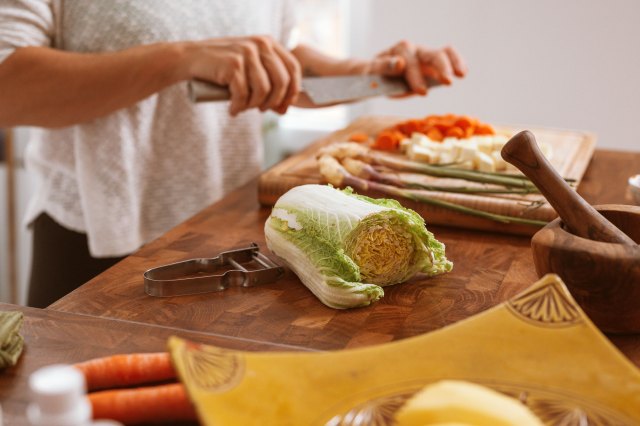 A person chops vegetables on a wooden cutting board