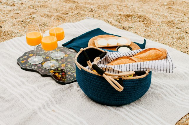 A picnic set up with a blanket on the sand, a bag full of supplies, and three glasses of an orange drink