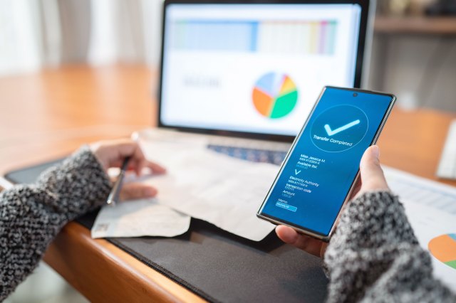 A woman looks at a computer monitor showing a budget while also looking at her phone