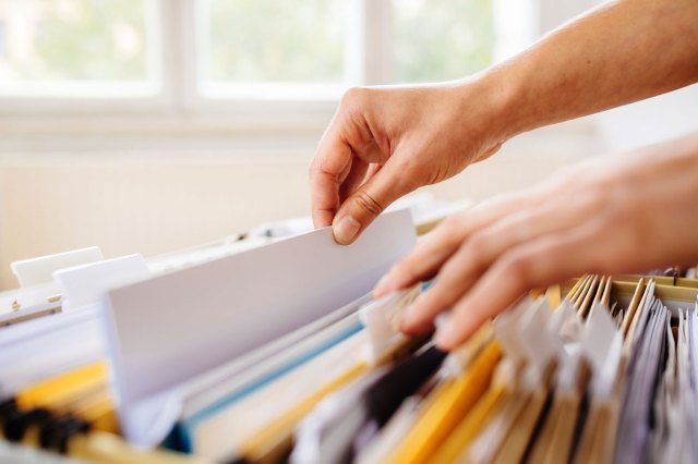 A pair of hands pull a file out of a filing cabinet