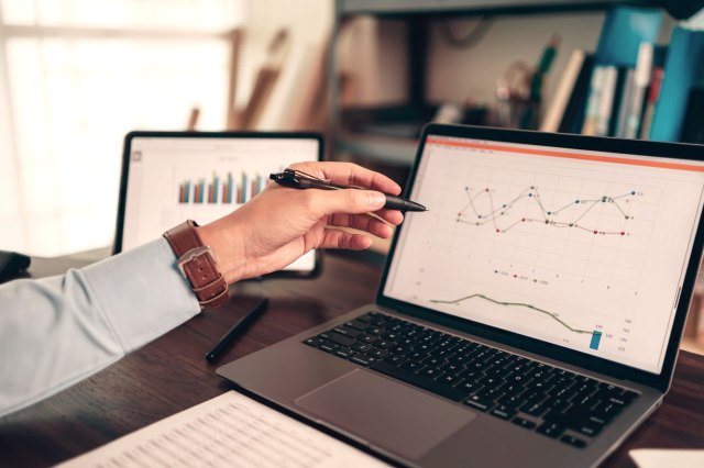 An image of a hand pointing to a computer screen with a graph on it