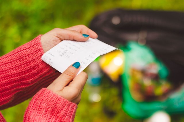 A pair of hands wearing blue nail polish hold a receipt