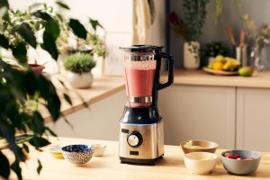 A blender sits on a countertop surrounded by bowls and plants