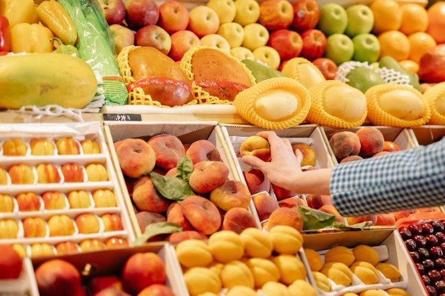 A hand selecting a peach from many different fruits