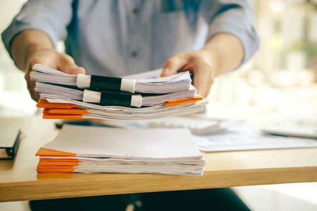 A man stacks large files on a wooden surface