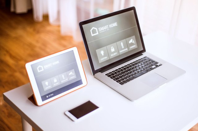 An open laptop, a tablet, and a phone sit on a white table