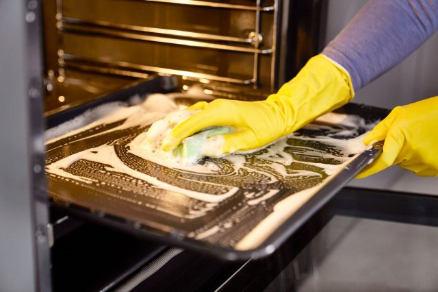 An image of a person wearing yellow rubber gloves cleaning a pan in the oven