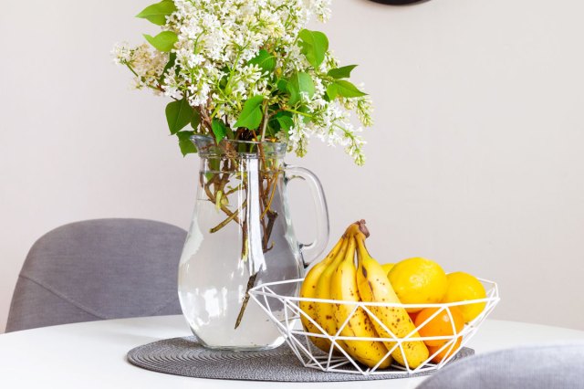 An image of a vase of flowers and a basket of fruit on a table