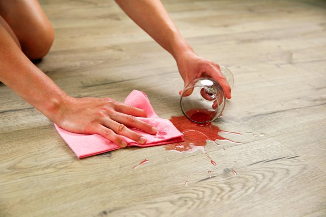 An image of a woman cleaning a wine spill on a wooden floor