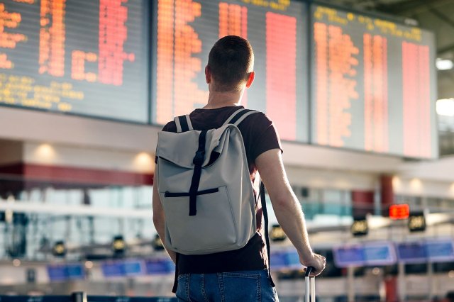 An image of a man wearing a backpack looking at a departure and arrival board at an airport