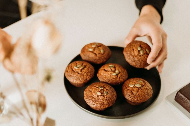 An image of a hand taking a muffin off a plate of muffins