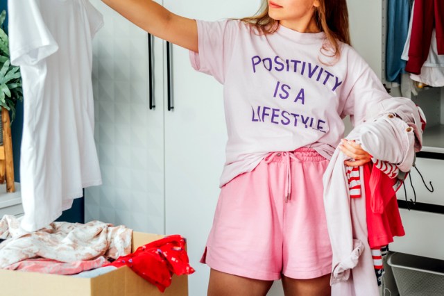 A woman examines a white t-shirt while holding other shirts over her other arm