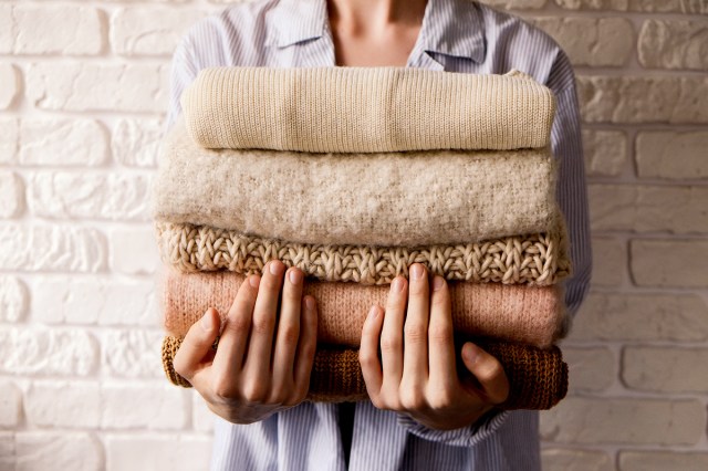 An image of a woman holding a stack of folded sweaters