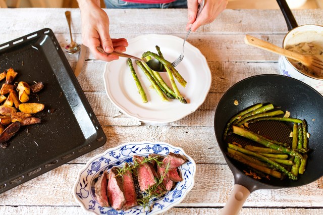 An image of a table with plates of asparagus, steak, and potatoes